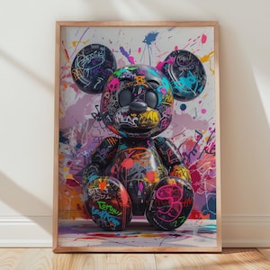 Peut inclure: Impression artistique encadrée d'un ours en peluche de style graffiti. L'ours est orné d'éclaboussures de peinture vives et d'art graffiti, avec des yeux et des oreilles noirs. L'œuvre est placée sur un fond blanc et encadrée de bois.