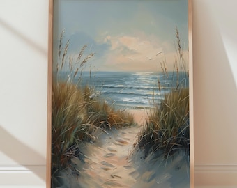 May include: A framed painting of a beach scene. The artwork shows a sandy path leading to the sea, framed by tall, dried grasses. The sky is a soft blue with hints of clouds, and the ocean reflects the sunlight. The frame is a light brown colour.