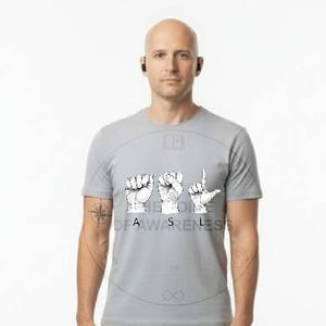 May include: A light gray t-shirt with the words "BE AWARENESS" in white, with hand gestures. The person is wearing khaki pants and white sneakers. The person is also wearing a black earbud.