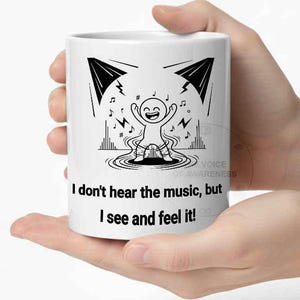 May include: White ceramic mug with a black and white illustration of a dancing stick figure with musical notes and the text "I don't hear the music, but I see and feel it!" A fun, music-themed gift.