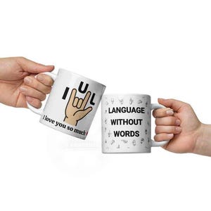 May include: Two white ceramic mugs with black text and graphics. One mug says "I love you so much" with a hand gesture. The other mug says "Language without words" with sign language symbols.
