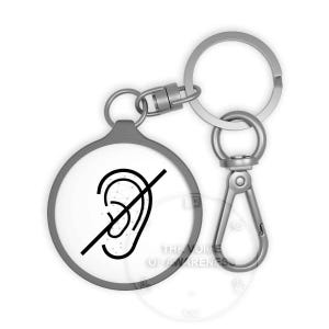 May include: A round, white keychain with a gray border and a silver keyring. The keychain features a black graphic of an ear with a line through it, indicating no sound. The text "THE VOICE OF AWARENESS" is visible.