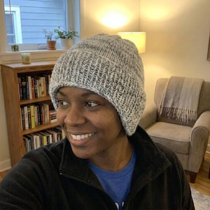 May include: A gray and white knit beanie hat. The hat is made of a thick, textured yarn and has a ribbed brim. The hat is designed to keep the head warm and is suitable for cold weather.