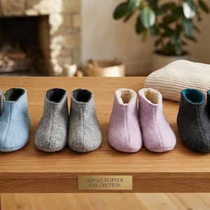 Puede incluir: Colección de zapatillas para adultos en varios colores, incluyendo azul claro, gris y lavanda, exhibidas sobre una superficie de madera. Las zapatillas tienen un diseño de botín con un interior suave y afelpado. El texto "ADULT SLIPPER COLLECTION" es visible.