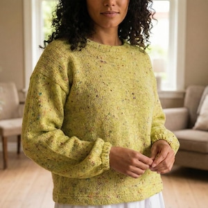 Könnte beinhalten: Ein hellgrüner Pullover mit Rundhalsausschnitt und langen Ärmeln. Der Pullover hat ein gesprenkeltes Muster mit bunten Flecken. Die Ärmel haben gerippte Bündchen. Das Kleidungsstück ist aus weichem Strick.