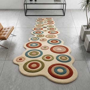 Könnte beinhalten: Ein cremefarbener, einzigartig geformter Teppich mit einem sich wiederholenden Muster aus farbenfrohen konzentrischen Kreisen. Die Kreise weisen Farbtöne von Rot, Blau, Grün und Rosa auf. Der Teppich liegt auf einem grau gefliesten Boden und verleiht dem Raum eine moderne Note.