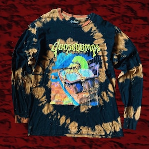 Peut inclure: Un t-shirt à manches longues noir avec un motif en spirale décoloré à l'eau de Javel. L'avant présente un graphique Goosebumps d'une créature dans une baignoire avec le texte "They're no yolk!" imprimé sous l'image. Col rond et poignets côtelés.