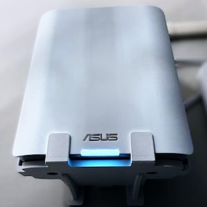 May include: A white ASUS router with a rectangular design. The router has a glowing blue light and the ASUS logo. The device has a modern, minimalist aesthetic and is designed for home or office use.