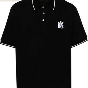 May include: Black polo shirt with white trim on the collar and sleeves. The shirt features a white embroidered logo on the chest and a three-button placket. The brand name "AMIRI" is visible on the collar.
