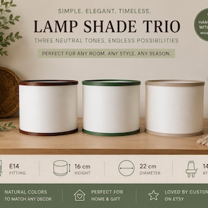 Peut inclure: Un trio d'abat-jours cylindriques avec des corps blancs et des bordures de couleurs différentes : marron, vert et beige. Les abat-jours mesurent 16 cm de haut et 22 cm de diamètre. Le texte indique "LAMP SHADE TRIO".