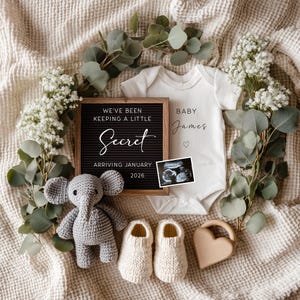 May include: A baby announcement with a white babygrow printed with "Baby James", a letter board reading "We've been keeping a little secret arriving January 2026", and a sonogram. The announcement includes a grey elephant toy, knitted baby shoes, and a wooden heart-shaped teether, surrounded by greenery and flowers.