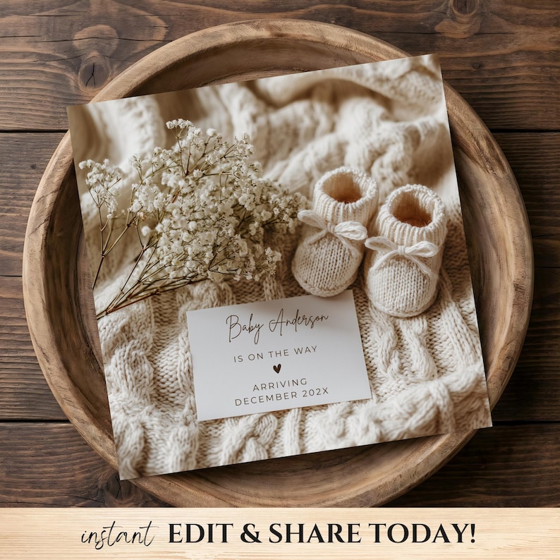 May include: A baby announcement card with the text "Baby Anderson is on the way, arriving December 202X" sits on a cream-colored knitted blanket. Two small, cream-colored knitted baby booties with bows are next to the card. A wooden bowl holds the items.