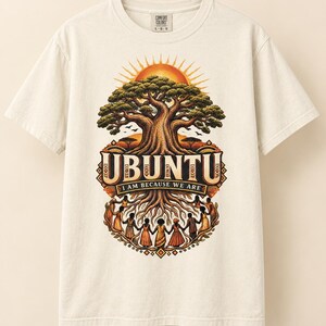 May include: An off-white short-sleeve t-shirt featuring a graphic of a large tree with a sun behind it. Below the tree, the text reads UBUNTU I AM BECAUSE WE ARE, with a circle of people holding hands forming the roots of the tree.