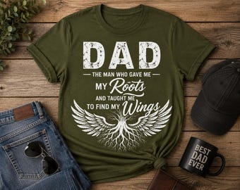 Op de afbeelding: Een olijfgroen T-shirt met korte mouwen en witte, verweerde tekst met de tekst DAD THE MAN WHO GAVE ME MY Roots AND TAUGHT ME TO FIND MY Wings boven een afbeelding van een boom met wortels en grote gevederde vleugels die uitsteken.