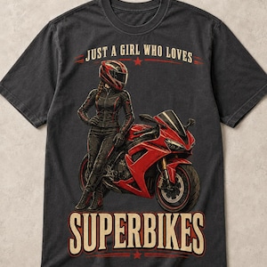 May include: A charcoal gray t-shirt featuring a graphic print of a person in a red helmet and black leather gear standing next to a red sport motorcycle. The text reads JUST A GIRL WHO LOVES at the top and SUPERBIKES at the bottom in bold letters.