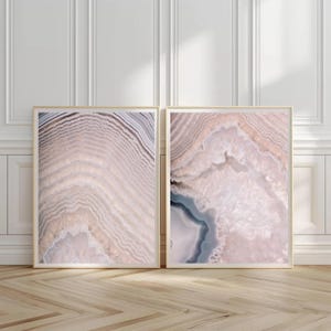 Peut inclure: Deux impressions d'art encadrées présentant des motifs de pierre d'agate en gros plan. Les impressions présentent des tons roses, beiges et gris. Les cadres dorés sont posés contre un mur blanc et un sol en bois.