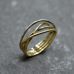 Puede incluir: Un anillo de oro y plata con múltiples bandas entrelazadas. El anillo está hecho de metal fino y tiene un diseño simple y moderno.