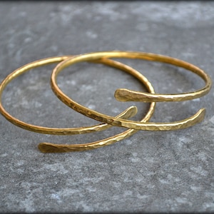 May include: Two gold-toned hammered metal bangles, stacked on top of each other.