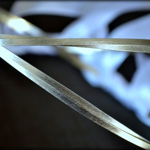 May include: Close-up of silver ribbon, with a metallic sheen, overlapping against a blurred white background. The ribbon appears to be thin and delicate, with a slight texture. The image is well-lit, highlighting the ribbon's reflective surface.