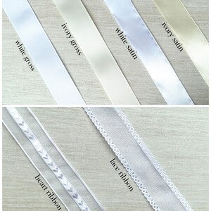 May include: Assortment of ribbons in various shades of white and ivory. The ribbons include white gross, ivory gross, white satin, ivory satin, heart ribbon, and lace ribbon. The ribbons are displayed diagonally against a light wood grain background.