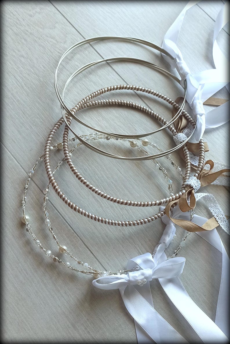 May include: A collection of wedding crowns with silver and gold tones. The crowns are adorned with pearls, ribbons, and bows. The design includes a twisted metal band and a delicate beaded strand.