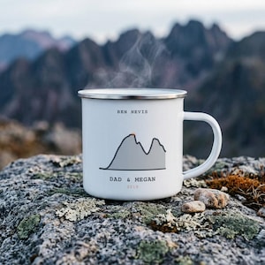 Può includere: Una tazza in smalto bianco con bordo argentato e manico. La tazza presenta un grafico di montagna grigio, il testo BEN NEVIS, DAD & MEGAN e l'anno 2019. Del vapore sale dalla parte superiore della tazza, riempita con una bevanda calda.
