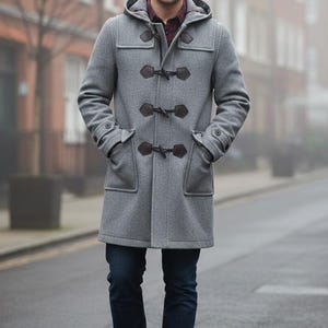 May include: A gray hooded duffel coat with dark brown toggles and pockets. The coat is worn with dark blue jeans and brown leather boots. The person is standing on a city street.