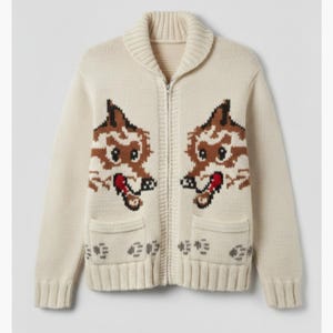 May include: Cream-colored zip-up cardigan sweater with a shawl collar and two front pockets. The sweater features a repeating pattern of two cartoon fox faces in brown, white, and red. The sweater is made of a knitted material.