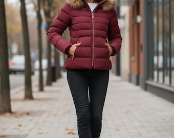 May include: A burgundy puffer jacket with a faux fur-trimmed hood and a gold zipper. The jacket is paired with black skinny jeans and black ankle boots. The woman is walking on a brick-paved sidewalk.