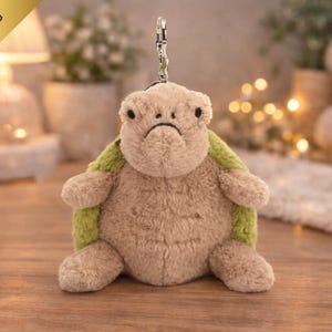 May include: A soft toy turtle keyring, featuring a beige body and green shell. The turtle has a downcast expression and a silver metal clip. The words "FREE SHIPPING" are printed on a gold banner in the upper left corner.
