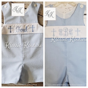 May include: Two light blue baby boy overalls with white trim. One has a cross and the name "Fond" embroidered on the front. The other has a cross and the monogram "BC" embroidered on the front. Both have the text "Klassic Kouture" on the bottom.
