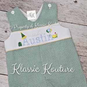 May include: Green and white gingham romper with white accents and embroidered details. The romper features the name "Austin" in blue script, along with golf-themed embroidery. The text "Klassic Kouture" is also visible.