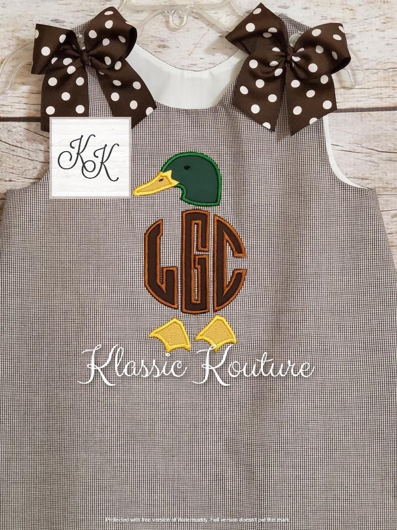 May include: A brown and white gingham sleeveless dress with a brown and white polka dot bow on each shoulder. The dress features an embroidered green duck with a brown monogram "LGC" and the text "Klassic Kouture".