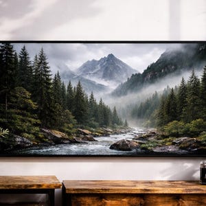 May include: A framed print of a mountain landscape with a river and evergreen trees. The artwork is displayed above a wooden table. A potted plant and a vintage camera are also visible in the image.