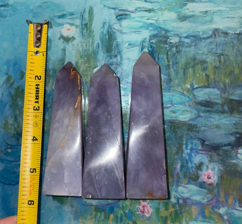 May include: Three purple crystal obelisks, each with a tapered shape and polished surface. The obelisks are approximately 5 inches tall. The crystals have a gradient of color, ranging from light lavender to deep violet.