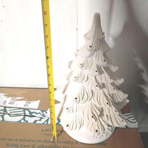 May include: A white ceramic Christmas tree with a textured surface. The tree is approximately 16 inches tall. It has multiple tiers and small holes for lights. The tree is sitting on a cardboard box.