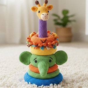 Op de afbeelding: Een handgemaakt gehaakt stapelspeelgoed met een giraffekop bovenop een leeuwenmanenring, gestapeld op een olifant met kleurrijke ringen. Het speelgoed is gemaakt van biologisch katoen en heeft de tekst "Handmade with Love & Organic Cotton".