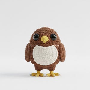 May include: A handmade crochet owl in shades of brown, white, and yellow. The owl has large black eyes, a yellow beak, and a white bib-like design on its chest. The owl's feet are yellow with grey accents.
