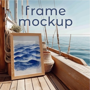 May include: A framed art print with a watercolor design of blue mountain ranges. The frame is light brown, and the artwork is displayed on a wooden surface with a nautical background. The text "frame mockup" is displayed in blue.