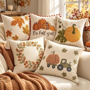 Peut inclure: Un ensemble de cinq coussins carrés en tissu crème. Les motifs incluent des feuilles d'érable orange, des citrouilles avec le texte 'It's Fall y'all', une grosse citrouille avec des vignes, une couronne de feuilles et un tracteur.
