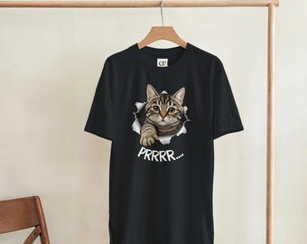 May include: Black t-shirt featuring a tabby cat graphic bursting through a torn hole. The cat has brown and tan fur, with the word "PRRRR..." printed below. The shirt is hanging on a wooden hanger.
