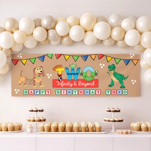 May include: A brown banner with cartoon characters and the text "TWO Infinity & Beyond Happy Birthday Theo". The banner is decorated with colorful pennants and balloons. Cupcakes are displayed on a white table.