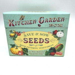 May include: A light blue rectangular storage box labelled Kitchen Garden Box. The front features illustrations of various vegetables, a butterfly, and a ladybug. Text reads: Save & Sow Seeds of Your Favourite Vegetables by Mike McGrath.