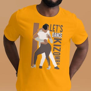 Peut inclure: T-shirt jaune moutarde avec un motif de deux danseurs enlacés. Le texte "LET'S DANCE KIZOMBA" est imprimé verticalement à droite. Les danseurs sont représentés en blanc, noir et gris.