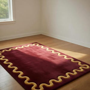 Puede incluir: Una alfombra rectangular de color burdeos con un borde ondulado de color amarillo dorado. La alfombra está colocada sobre un suelo de madera en una habitación con una ventana. El diseño de la alfombra añade un toque de elegancia a la decoración de la habitación.