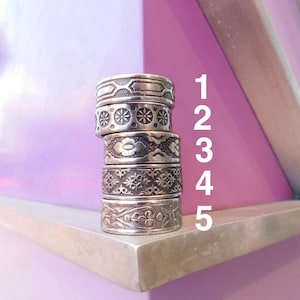 May include: A vertical stack of five silver-toned metal rings, each featuring a distinct embossed pattern. The rings are numbered 1 through 5 in white text to the right of the stack. The top ring has a geometric design, followed by floral and intricate motifs.