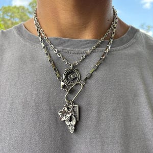 Puede incluir: Un conjunto de collares plateados superpuestos que incluye una cadena fina de eslabones redondos y una cadena m&aacute;s gruesa de eslabones rectangulares. Incluye un colgante circular con dise&ntilde;o grabado y un cierre de mosquet&oacute;n con un dije floral.