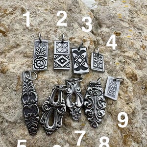 Puede incluir: Una colecci&oacute;n de nueve colgantes de metal plateado con varios patrones en relieve, incluyendo dise&ntilde;os florales, geom&eacute;tricos y volutas ornamentadas. Cada colgante est&aacute; numerado del uno al nueve e incluye una peque&ntilde;a anilla de metal.