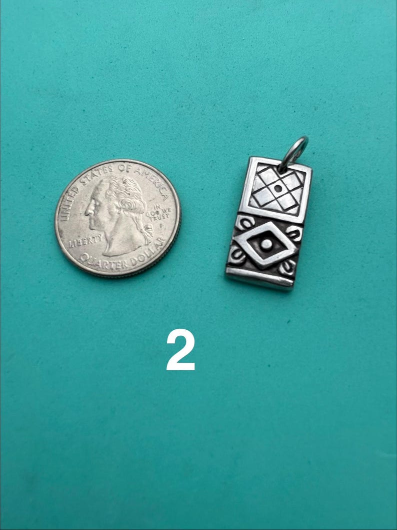 Puede incluir: Un colgante rectangular de plata con un patr&oacute;n geom&eacute;trico grabado que presenta una cuadr&iacute;cula cuadrada en la parte superior y una forma de diamante en la parte inferior, junto a una moneda de cuarto de d&oacute;lar estadounidense. El n&uacute;mero 2 aparece debajo.