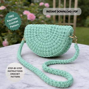 May include: A mint green crochet handbag with a matching strap. The bag has a half-moon shape and gold-colored hardware. Text on the image reads "FREE Keychain Crochet Pattern" and "STEP-BY-STEP INSTRUCTIONS CROCHET PATTERN". The text "INSTANT DOWNLOAD | PDF" is also visible.